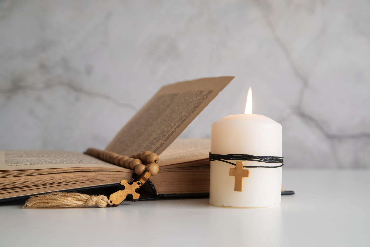Otvorena Biblija s krunicom i svijećom koja gori na kojoj je križ - simbolički označava čitanje poglavlja dnevne liturgije odnosno evanđelje dana.